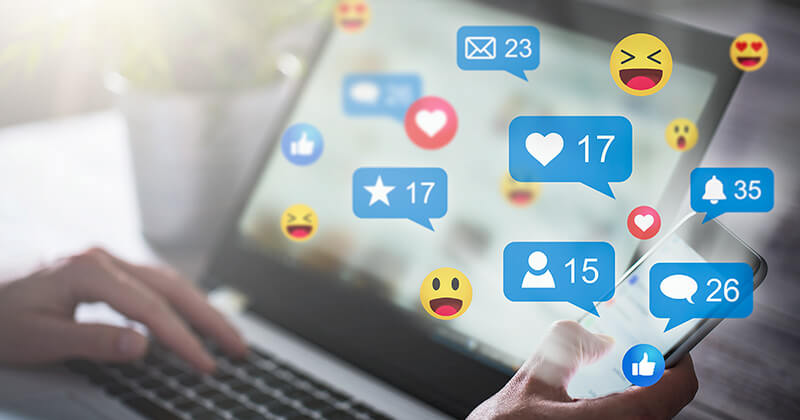 Person interacting with social media on laptop and smart phone. Social media icons are displayed.