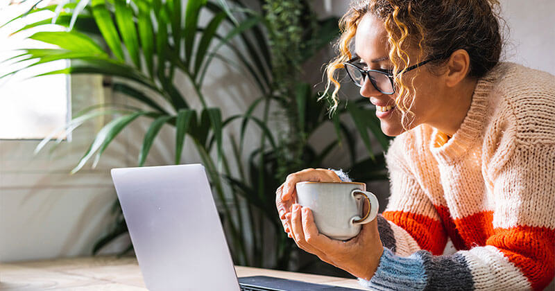 Woman holding a coffee cup browsing on a laptop.
